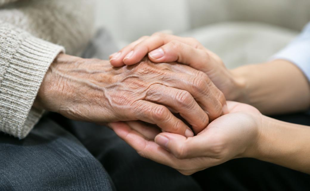 Mãos de uma pessoa idosa acolhidas por uma pessoa mais jovem